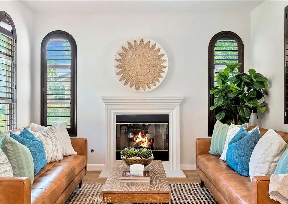 Living room with two leather sofas, coffee table, fireplace, wall art, windows, and plant