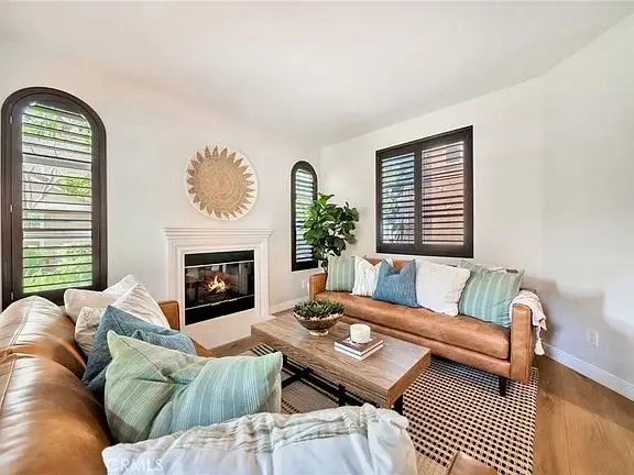Living room with brown leather sofa, decorative pillows, wooden coffee table, fireplace, windows