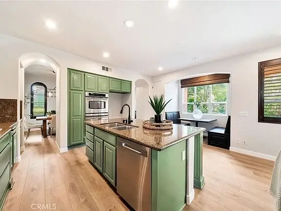 Kitchen with green cabinets, central island with granite countertop, stainless steel appliances, and windows
