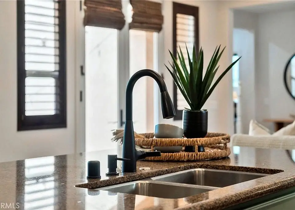 Kitchen sink with black faucet, potted plant, woven basket, and natural light from windows