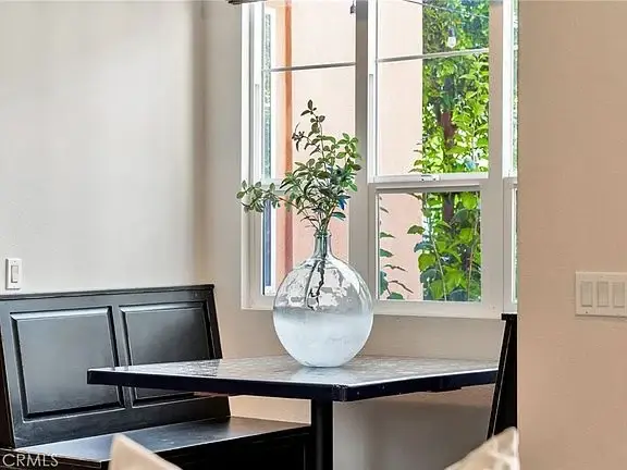 Table with glass vase and plant, window with greenery outside, and black built-in bench