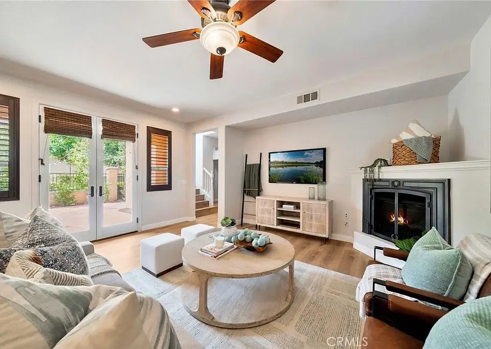Living room with ceiling fan, comfortable seating, round coffee table, fireplace, TV, and windows and doors to outdoor space