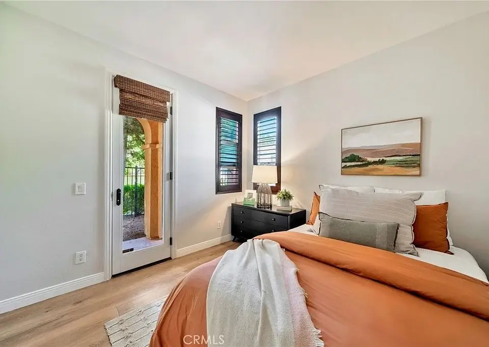 Bedroom with a bed in orange and white bedding, a nightstand with a lamp, wall art, and a door with windows on each side.