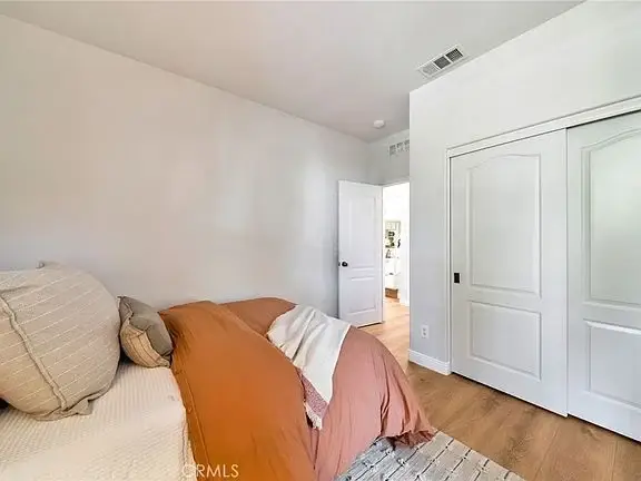 Bedroom with a bed, orange and white bedding, light-colored walls, and a closet door
