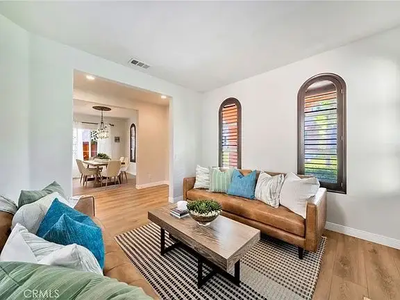 Living room with brown leather sofa, decorative pillows, wooden coffee table, fireplace, windows with shutters, and a plant