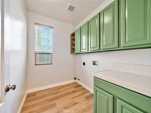 Room with green cabinets, tiled countertop, window with blinds, and wood-like floor