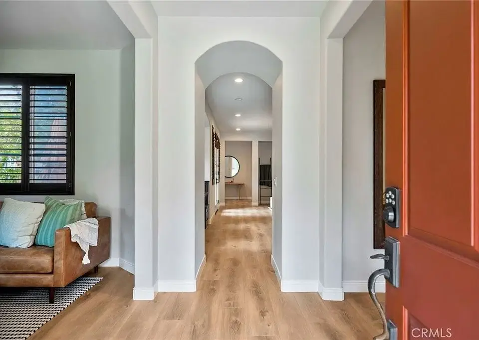 Hallway with wooden floor, arched entryway, brown couch, and light-colored walls