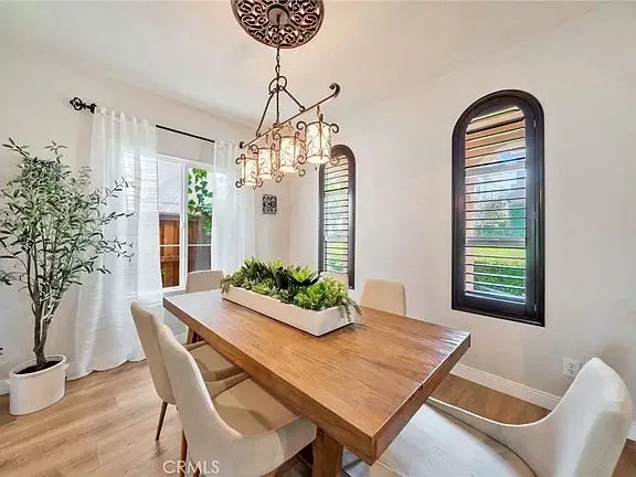 Dining area with wooden table, four white chairs, plant centerpiece, arched black windows