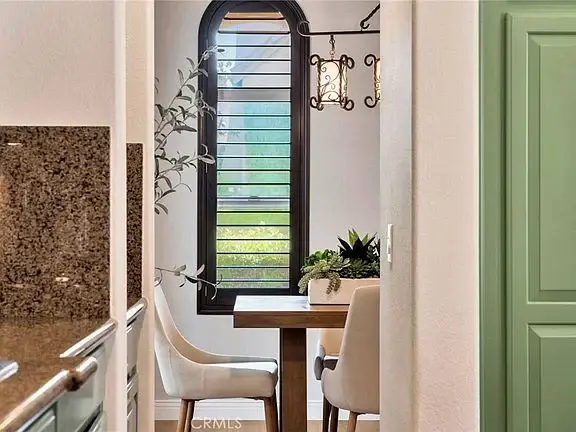 Dining area with wooden table, two white chairs, plant on table, window, and green cabinets in background