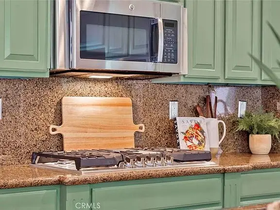 Kitchen with green cabinets, microwave above stovetop, wooden cutting board, and decorative items on counter
