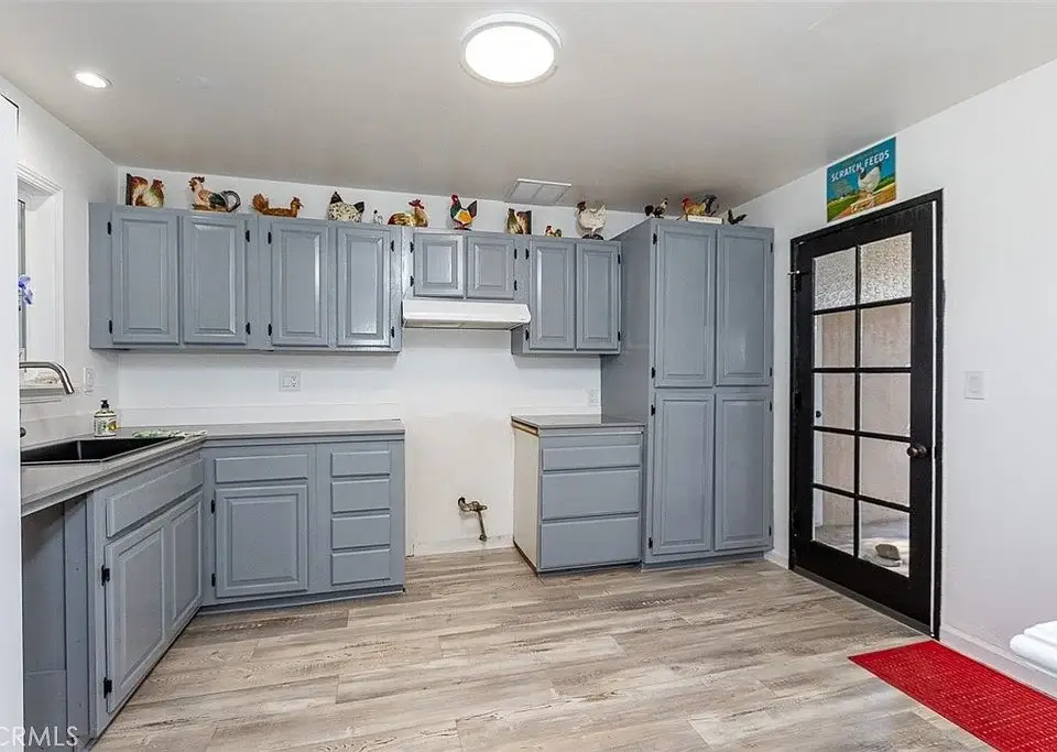Kitchen with gray cabinets, black countertop, black glass-panel door, light-colored floor, and decorative items on cabinets.