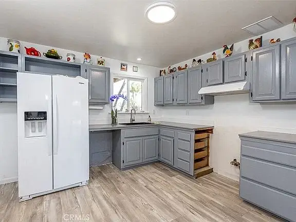 Kitchen with gray cabinets, white refrigerator, wooden floor, decorated shelves, and window