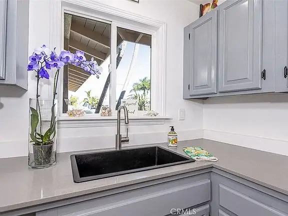 Kitchen sink area with dark sink, gray cabinets, window, and orchid in a vase on the countertop.