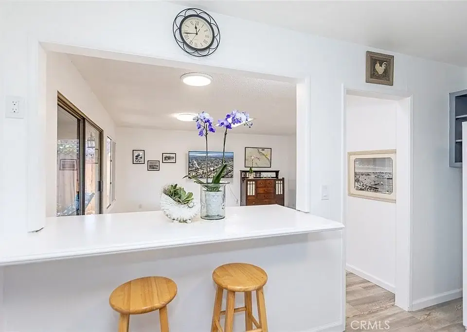 interior space with bar counter, two wooden stools, purple orchids, and view into another room with artwork.