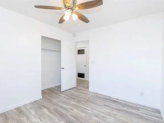 empty room with white walls, light wood floor, ceiling fan, open closet, and closed entrance door.