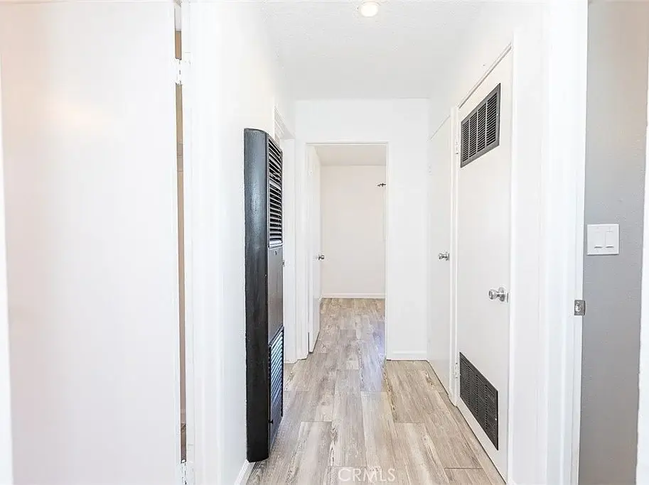 hallway with white walls, light wood floor, doors to rooms