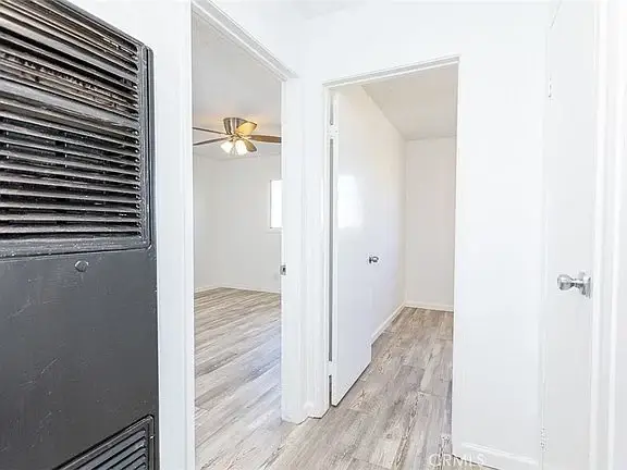 Hallway with white walls, light wood floor, doorway to a room, and another door on the right.