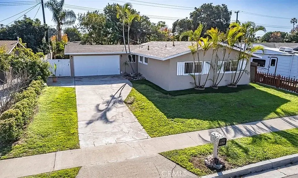 Single story California real estate house with garage, paved driveway, palm trees, and green yard.