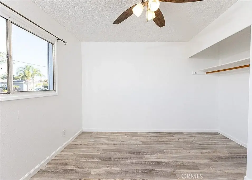 Vacant room with light walls, wooden floor, ceiling fan, window, and open closet.