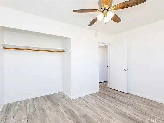 empty room with light walls, wooden floor, ceiling fan, open closet, and a closed door.