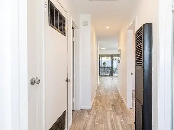 Hallway with white walls, light wooden floors, closed doors, and a room at the end.