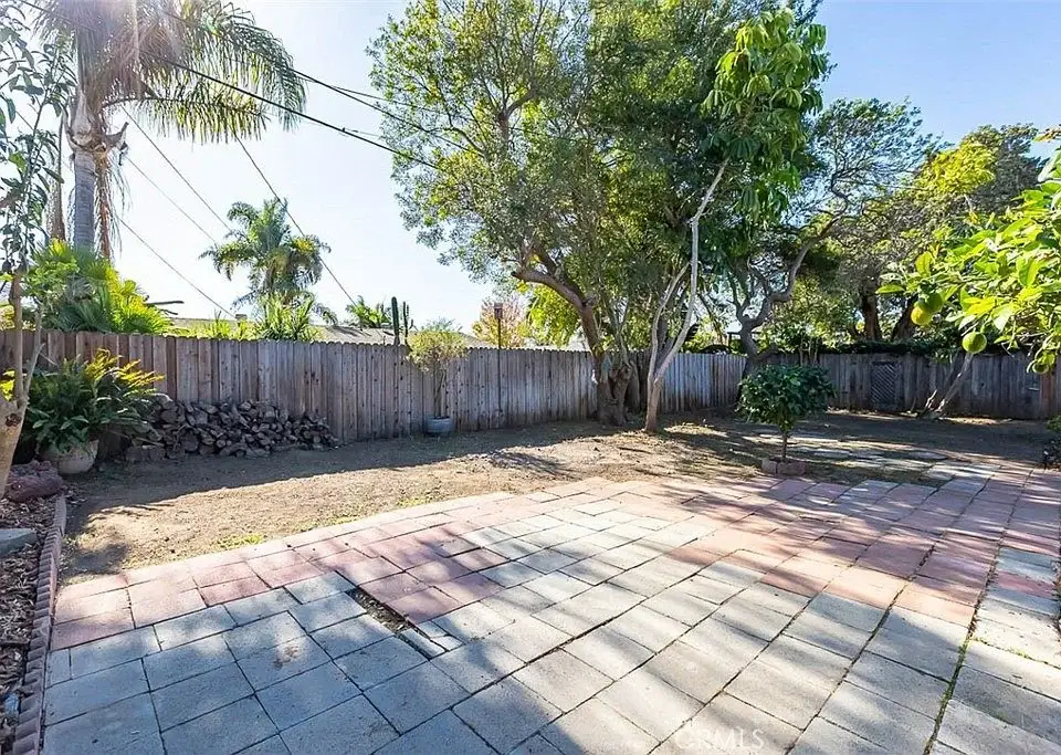 Spacious backyard with a stone patio, trees, and a wooden fence.
