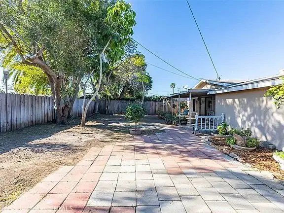 Backyard with paved area, trees, and a California real estate house in the background.