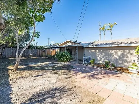 Residential area with a single-story California real estate house, brick pathway, and trees in the yard.