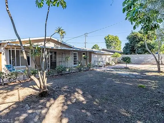 Backyard with trees, patio, landscaping, and a single-story California real estate house in the background.