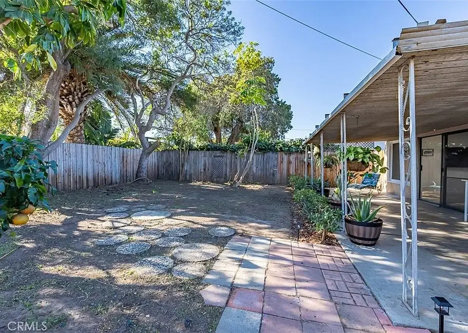 Backyard with dirt, trees, wooden fence, stone stepping stones, brick paths, and potted plants