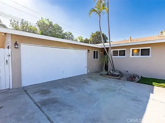 Driveway to house California real estate with garage, palm trees, and yard.