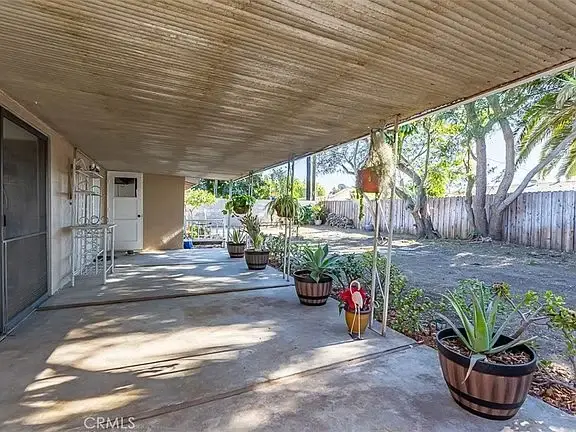 Covered patio with potted plants and a grassy backyard.