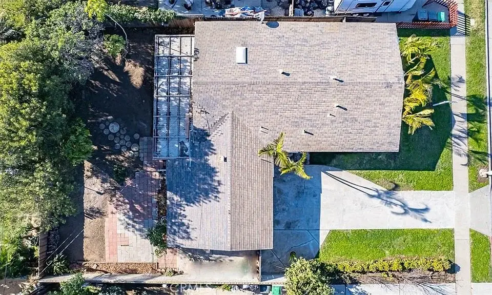 Aerial view of a California real estate house with a large backyard, trees, and green grass.