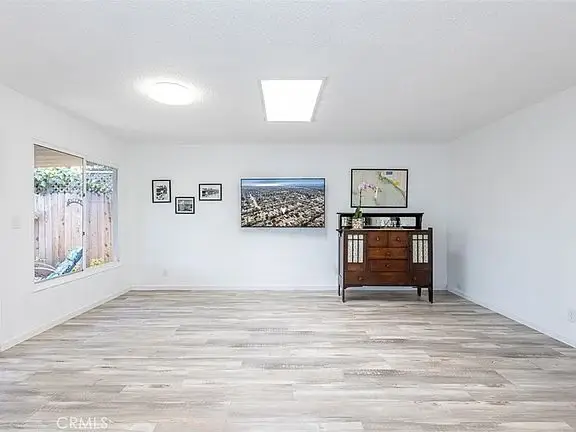 Empty room with wood floor, light walls, big windows, wall photos, and wood cabinet.