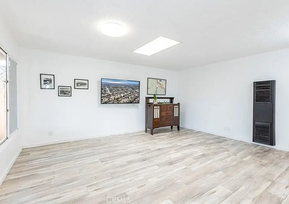 Room with wood floor, white walls, big window, wall photos, screen display, and wood cabinet.