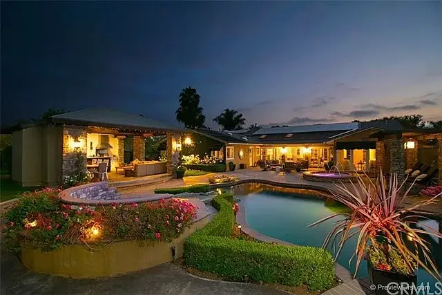 Backyard of house California real estate with pool, outdoor lights, tropical plants, and house.