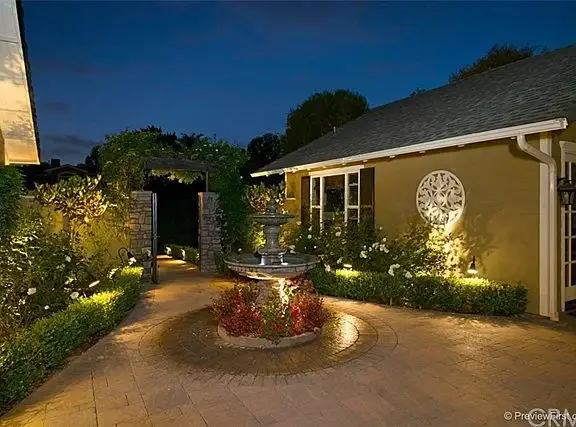 Garden pathway of house California real estate with fountain, flowers, hedges, and walkway lights.