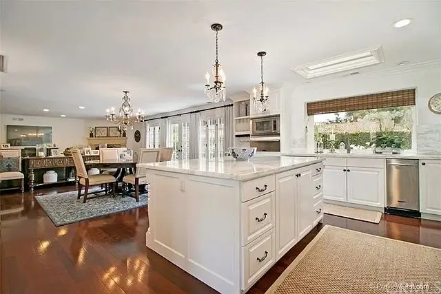 Kitchen with white cabinets, island, pendant lights, dining area, hardwood floor, and large windows.