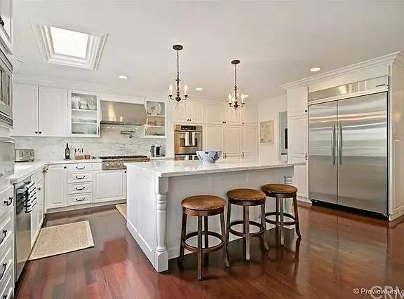 Kitchen with white cabinets, stainless steel appliances, center island with bar stools, hardwood floor