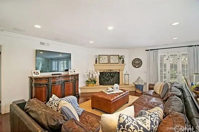Living room with brown leather sofa, wooden coffee table, fireplace, wall TV, and large windows.