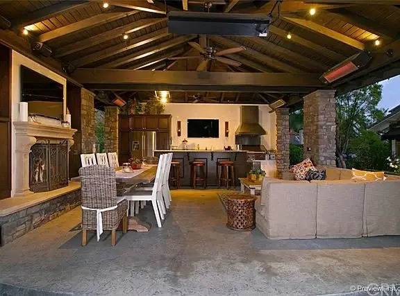 Patio of house California real estate with stone fireplace, dining table, bar, seating, and wood roof lights.