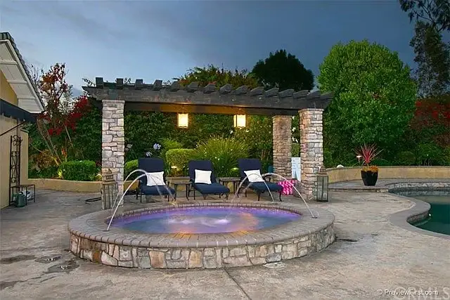Backyard of house California real estate with stone hot tub, pergola, lounge chairs, lights, and plants.