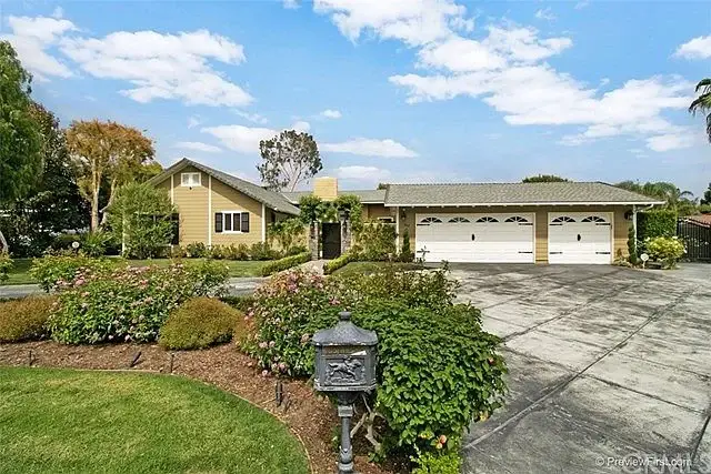 Large luxury house California real estate with beige exterior, plants, flowers, yard, driveway, and three car garage.