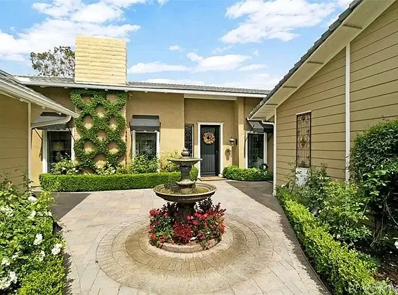 House California real estate front entrance with black door, wreath, sidelights, lantern, doormat, greenery, and flowers.