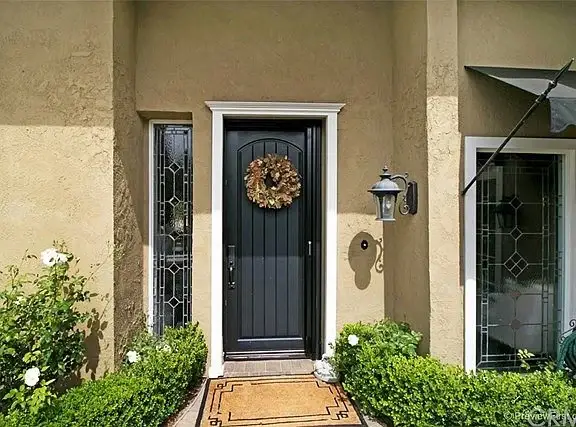 House California real estate front door with wreath, side windows, bushes, and doormat.