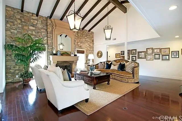 Living room with stone fireplace, wood beam ceiling, couch, armchairs, and decor.